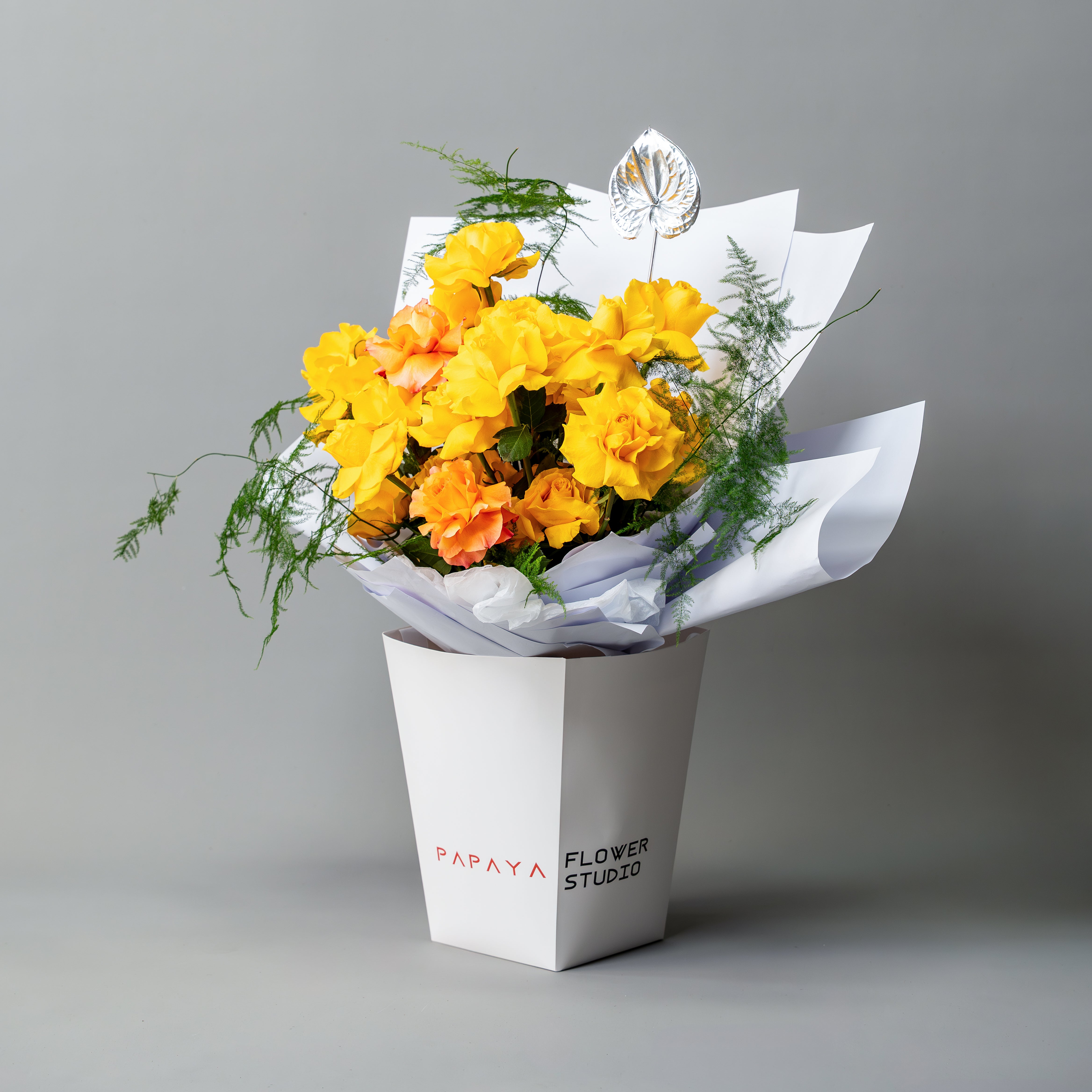Bright yellow reflexed roses bouquet with silver anthurium leaf in white branded carrier box delivery Dubai.