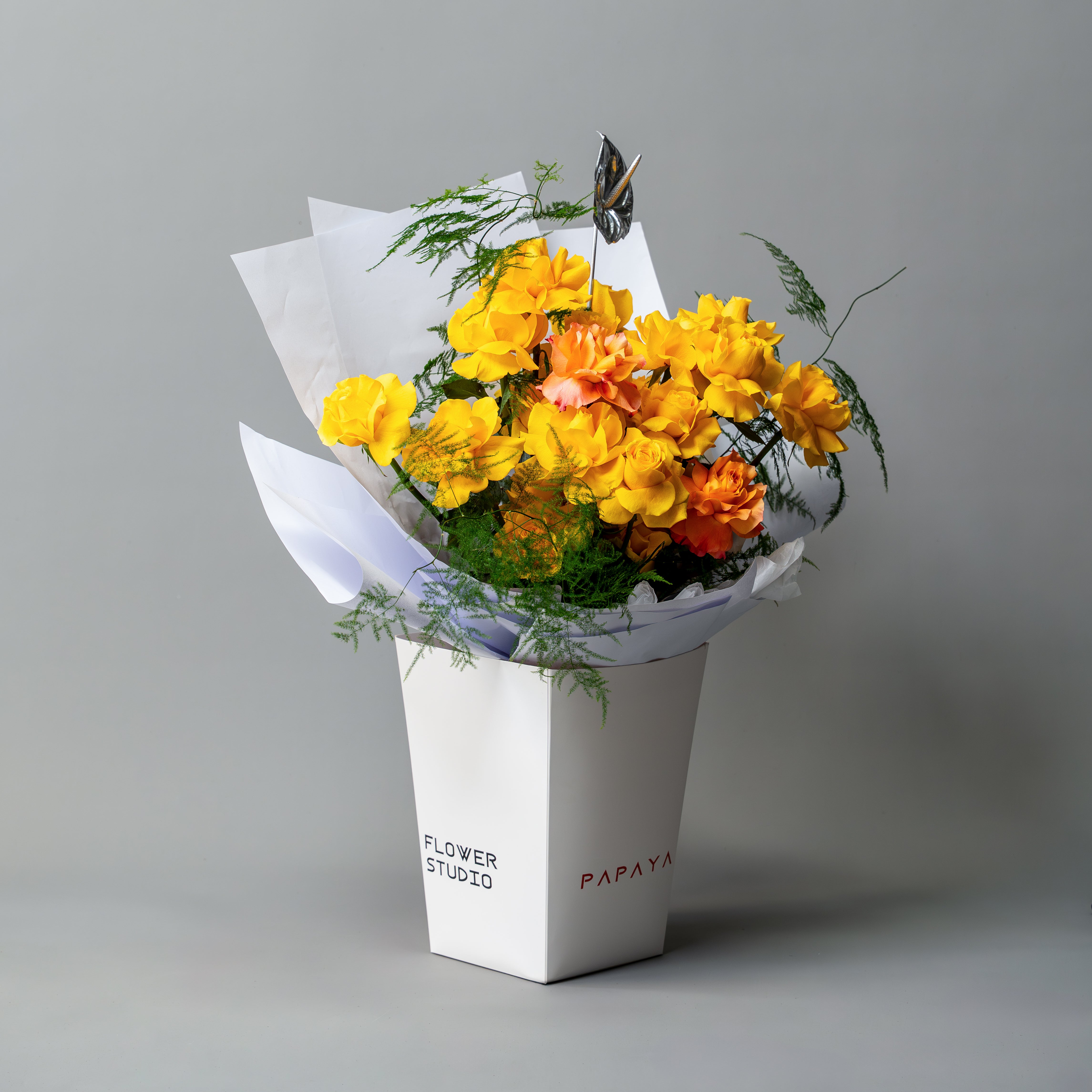 Bright yellow reflexed roses bouquet with silver anthurium leaf in white branded carrier box delivery Dubai.
