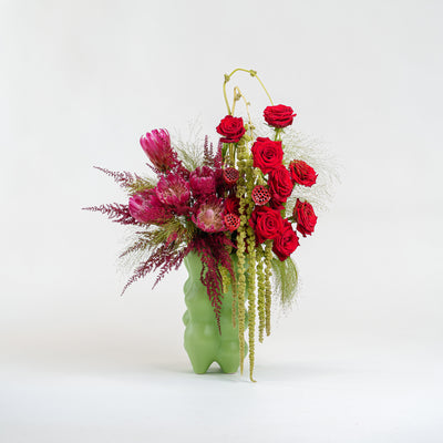Floral arrangement with red and pink flowers in a green vase on a white background