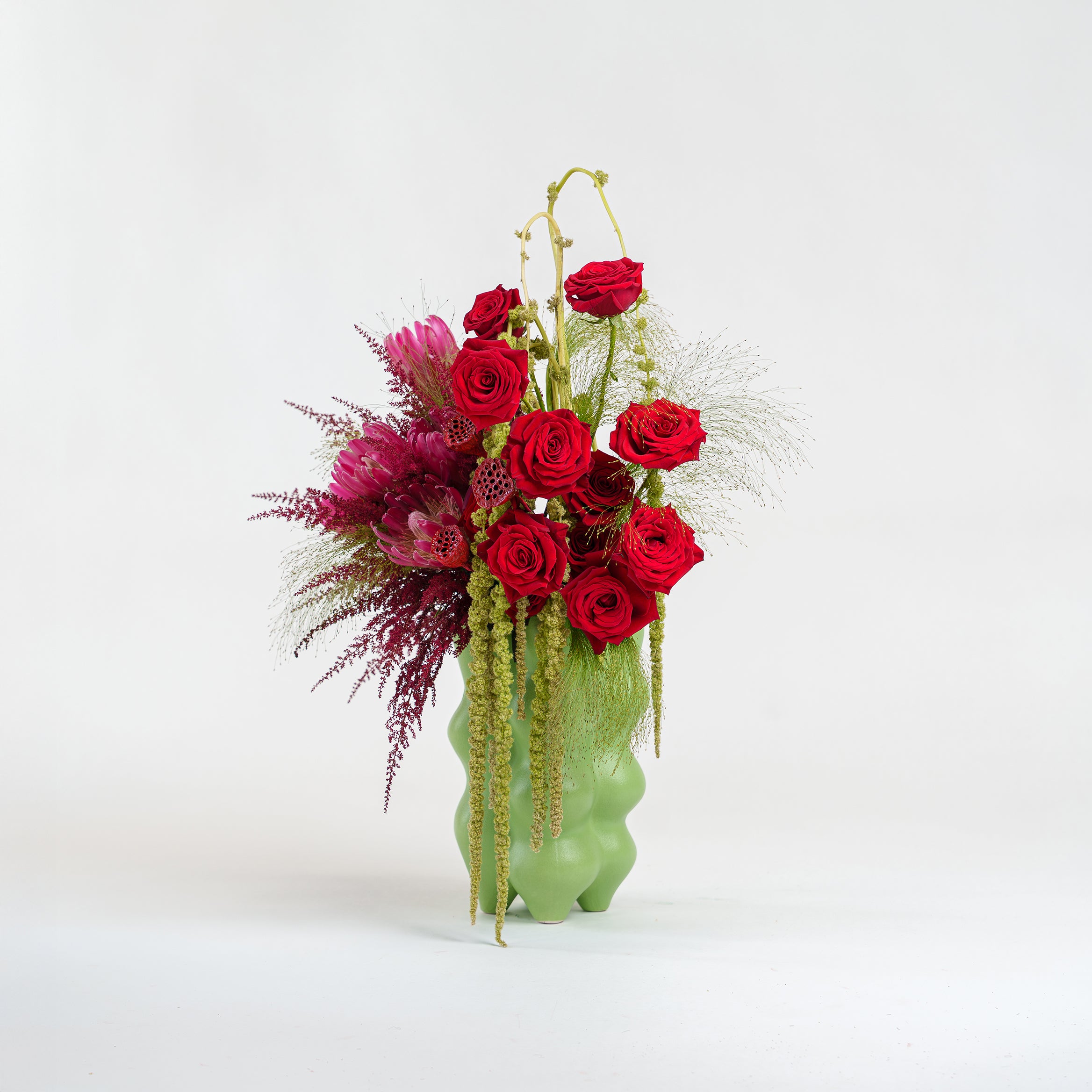 Floral arrangement with red roses and greenery in a green vase on a white background
