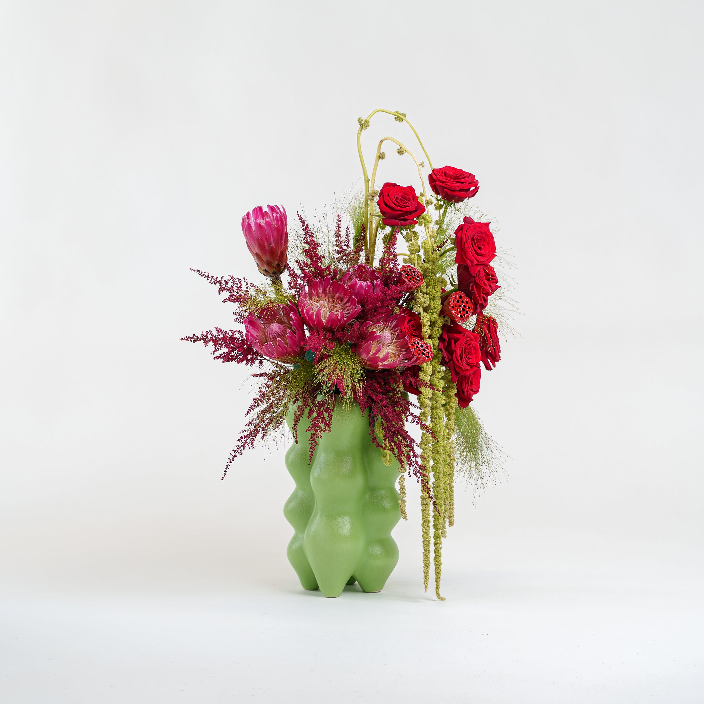 Green vase with a colorful flower arrangement on a white background