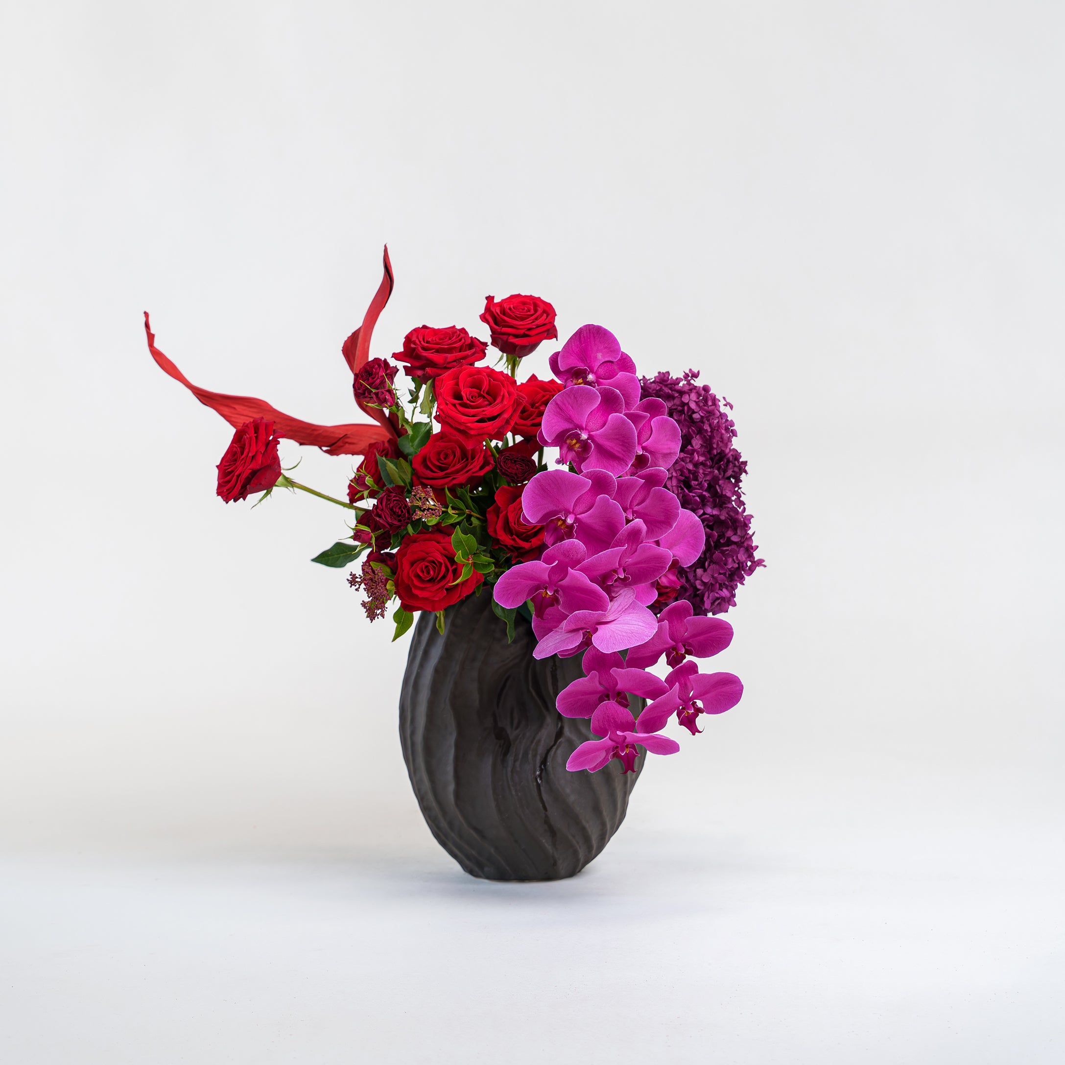 Floral arrangement with red roses and pink orchids in a black vase on a white background