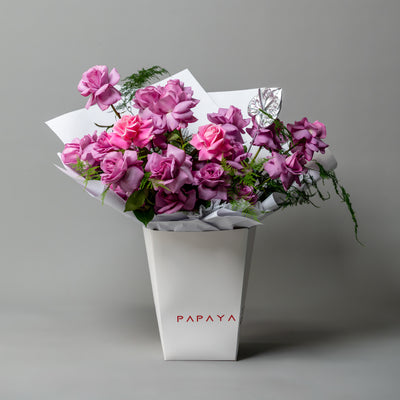 Vibrant bouquet of purple and pink reflexed roses with silver anthurium leaf in white branded carrier box delivery Dubai.