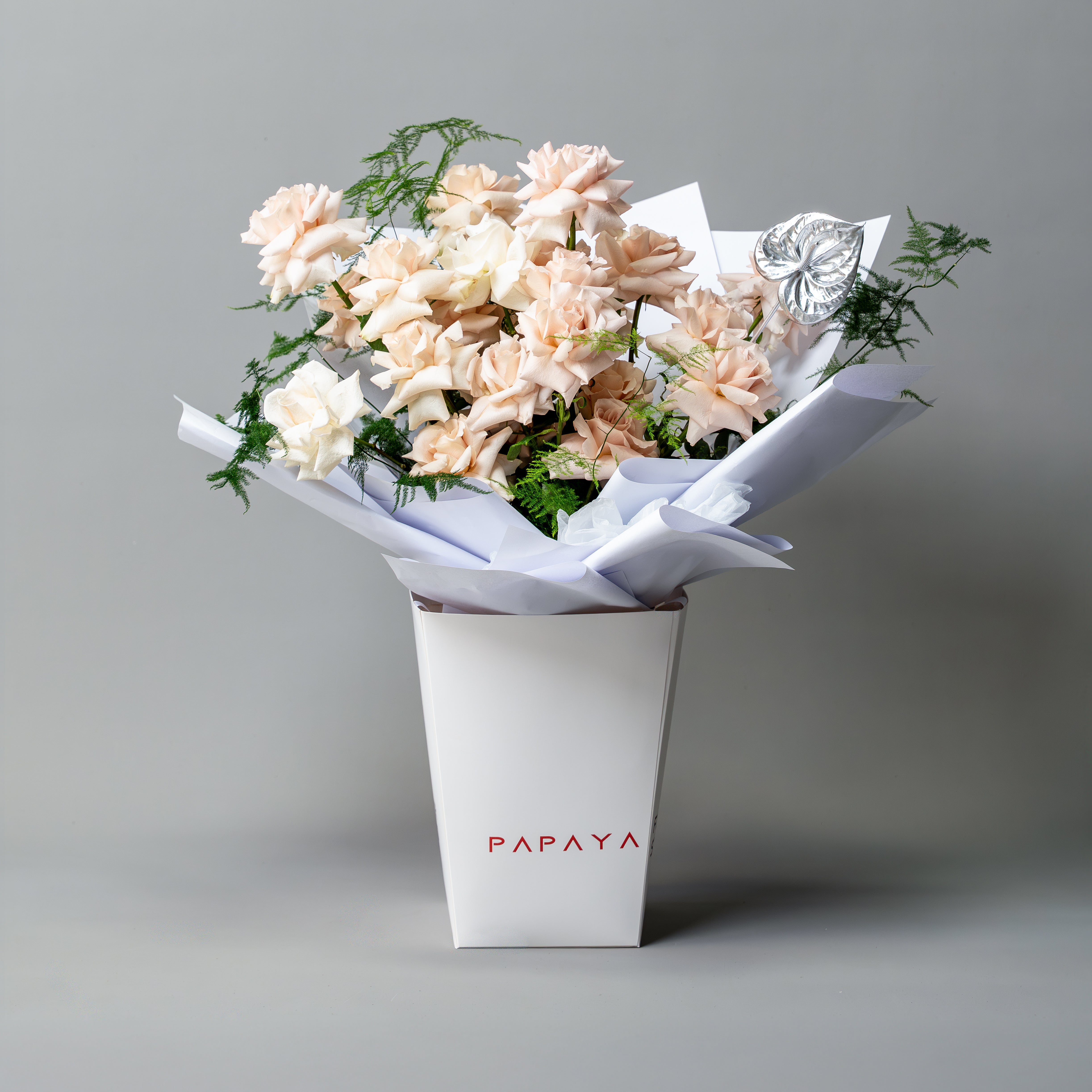 Modern bouquet of nude and champagne sand-colored reflexed roses with silver anthurium leaf in white branded carrier box delivery Dubai