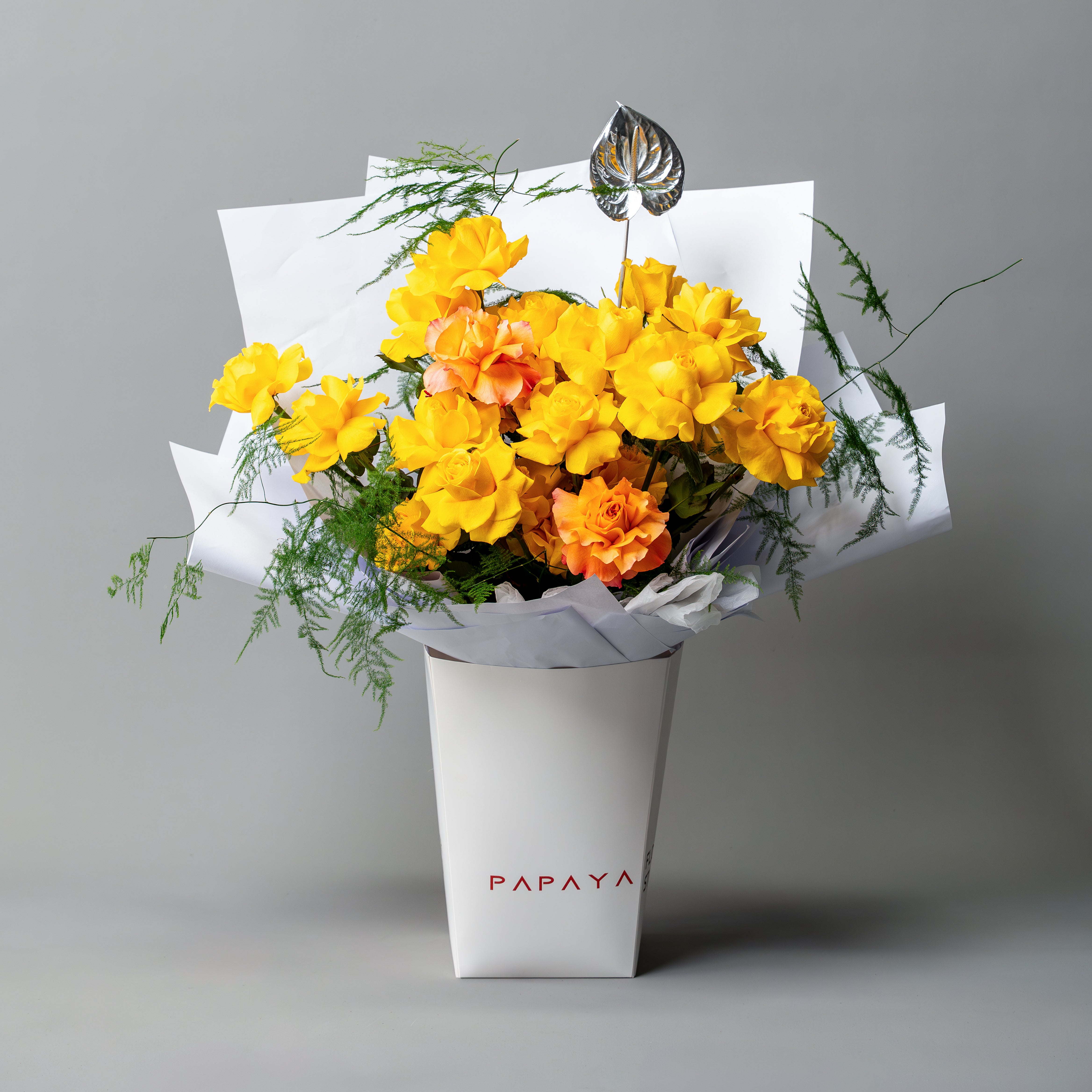 Bright yellow reflexed roses bouquet with silver anthurium leaf in white branded carrier box delivery Dubai.