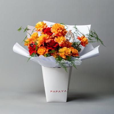 Vibrant bouquet of fiery orange and red reflexed roses with silver anthurium leaf in white branded carrier box delivery Dubai.