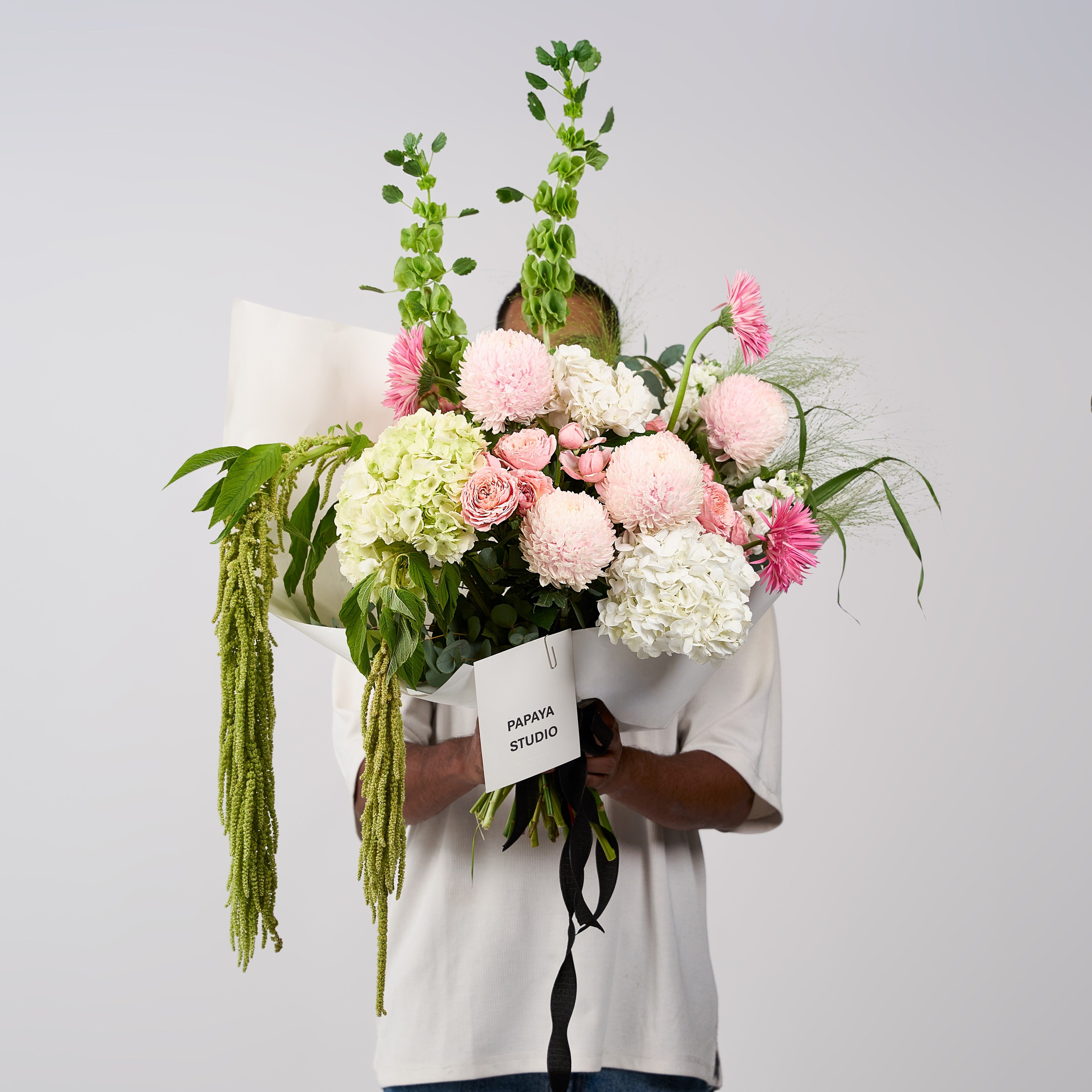 Soft pink and ivory flower bouquet with cascading greenery, tall green stems, ivory wrapping and a black ribbon.