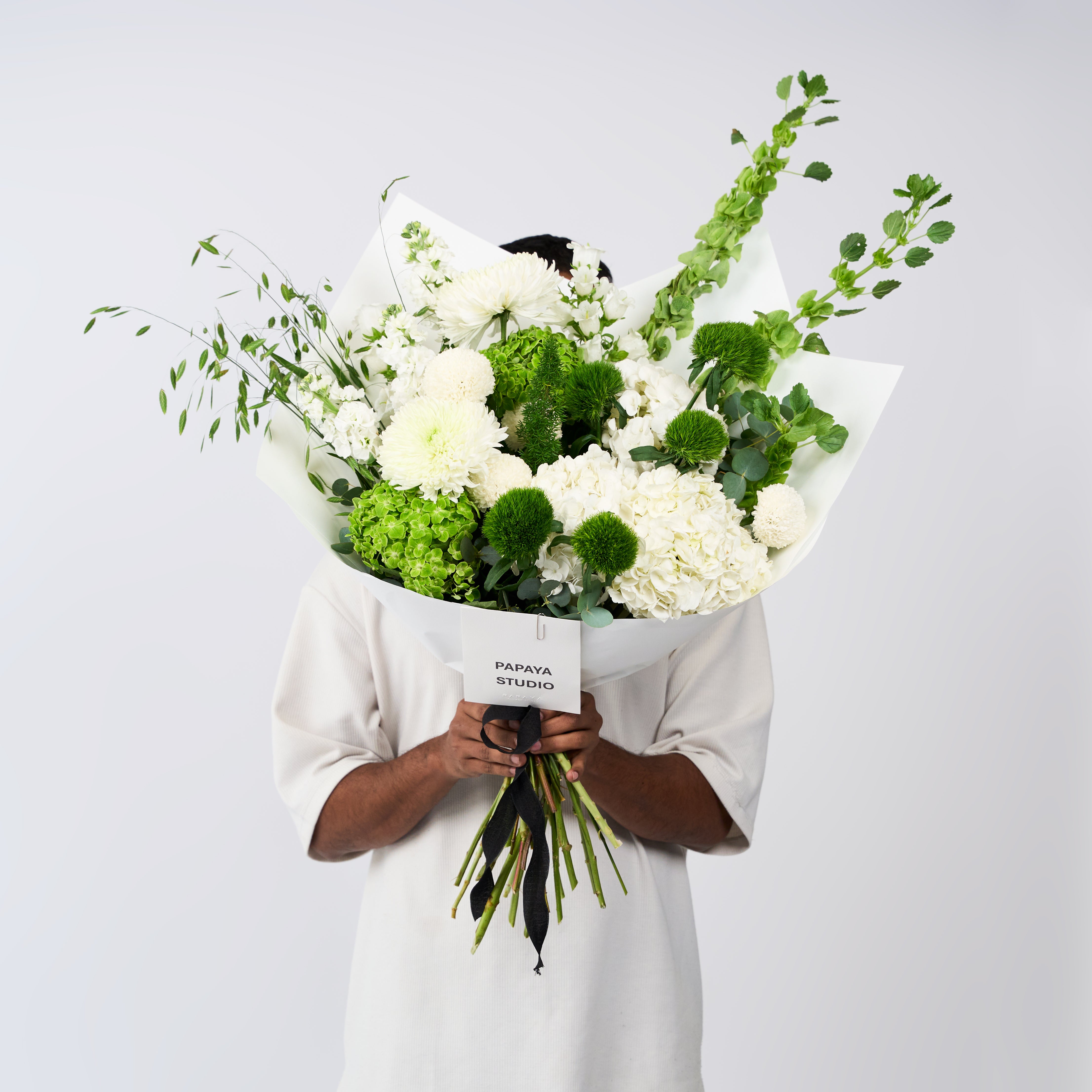 White and green flower bouquet with hydrangeas, rounded blooms, tall green stems, ivory wrapping and a black ribbon.