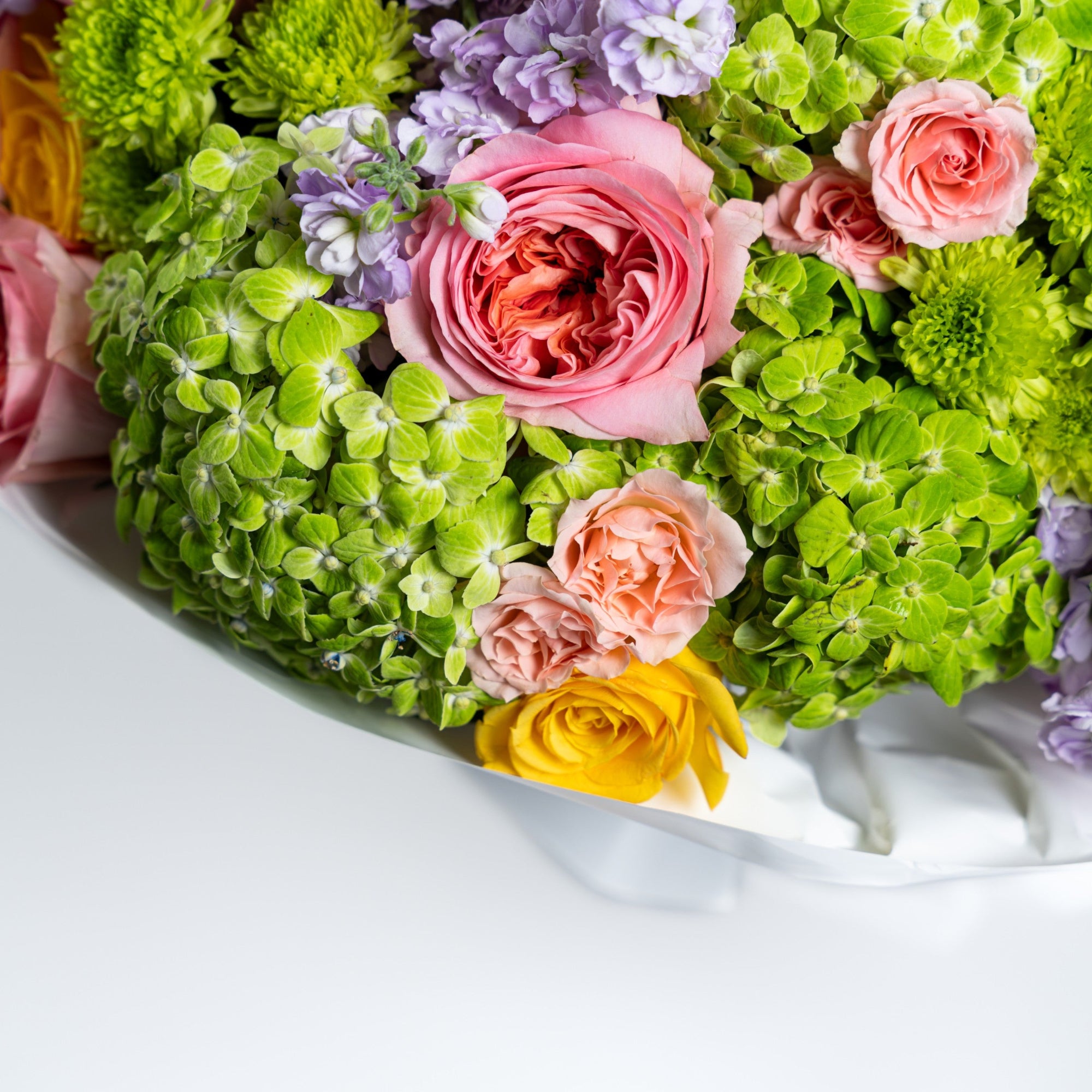 Detailed view of a pink garden rose, peach spray roses, green hydrangeas and chrysanthemums