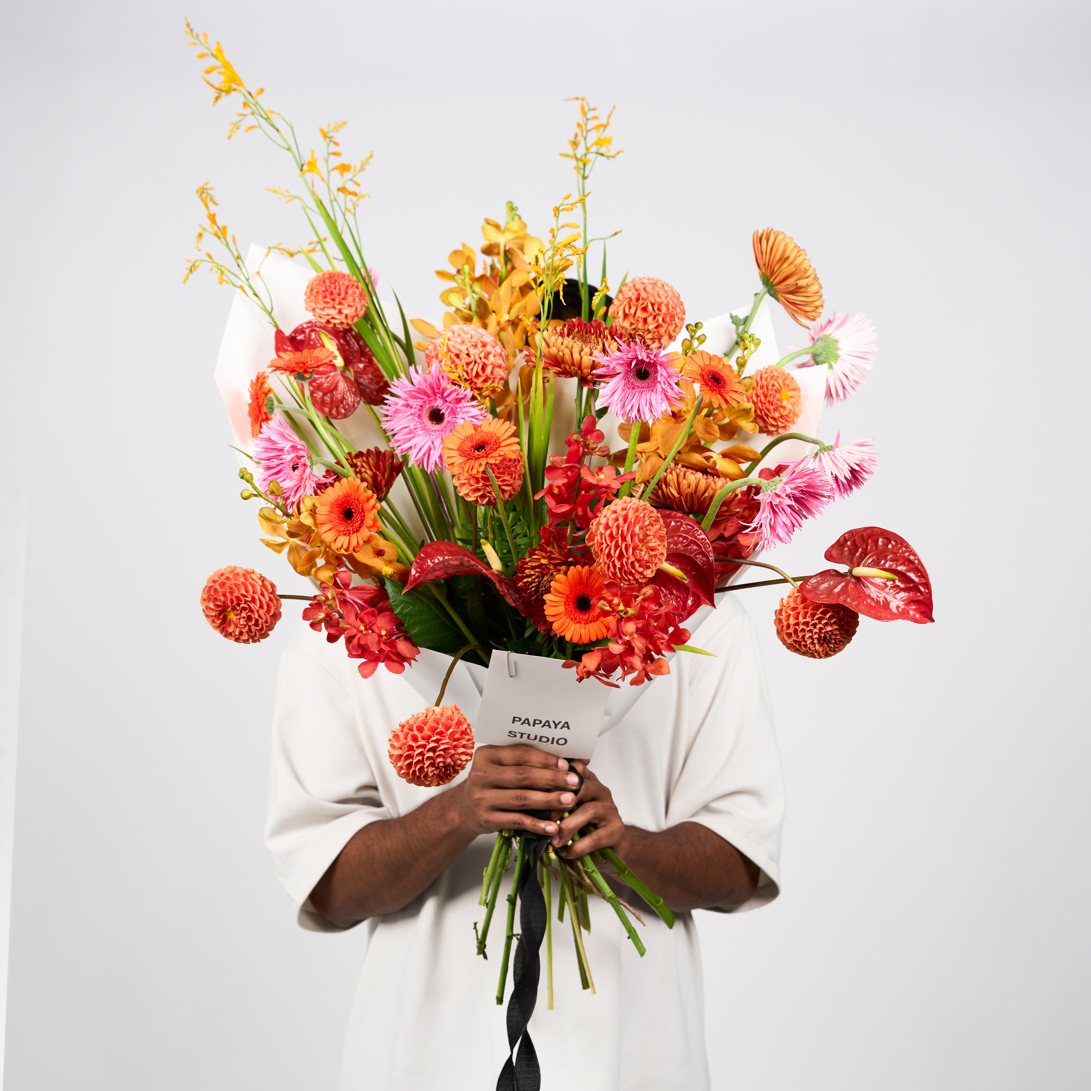 Orange, coral and pink flower bouquet with golden accents, tall stems, ivory wrapping and a black ribbon
