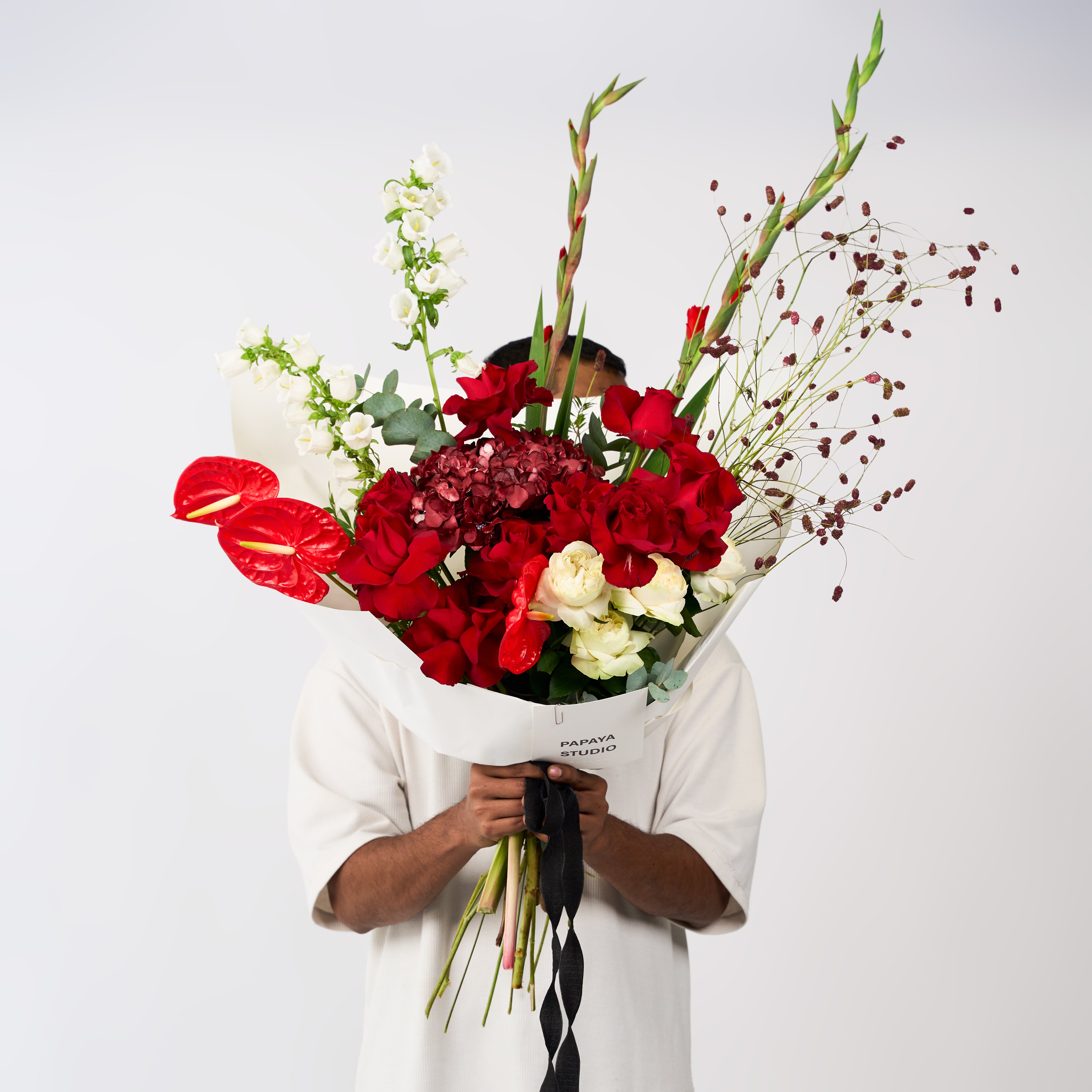 Red rose and ivory flower bouquet with burgundy accents, airy branching stems, ivory wrapping and a black ribbon.