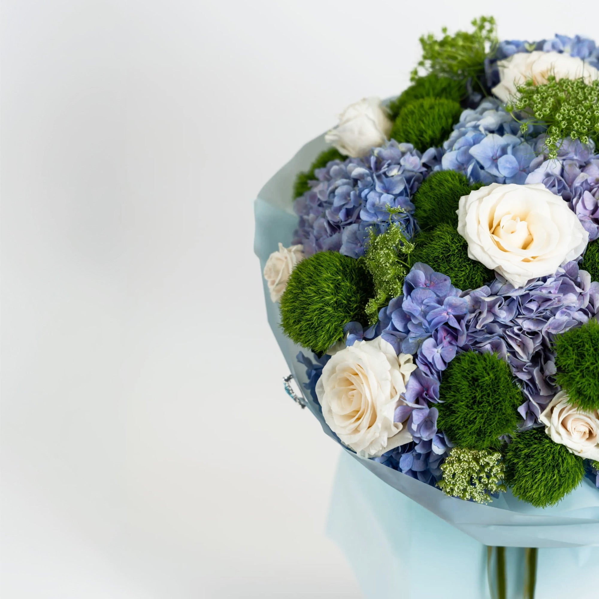 Close-up of blue hydrangeas, ivory roses and green dianthus in The Azure Reverie bouquet