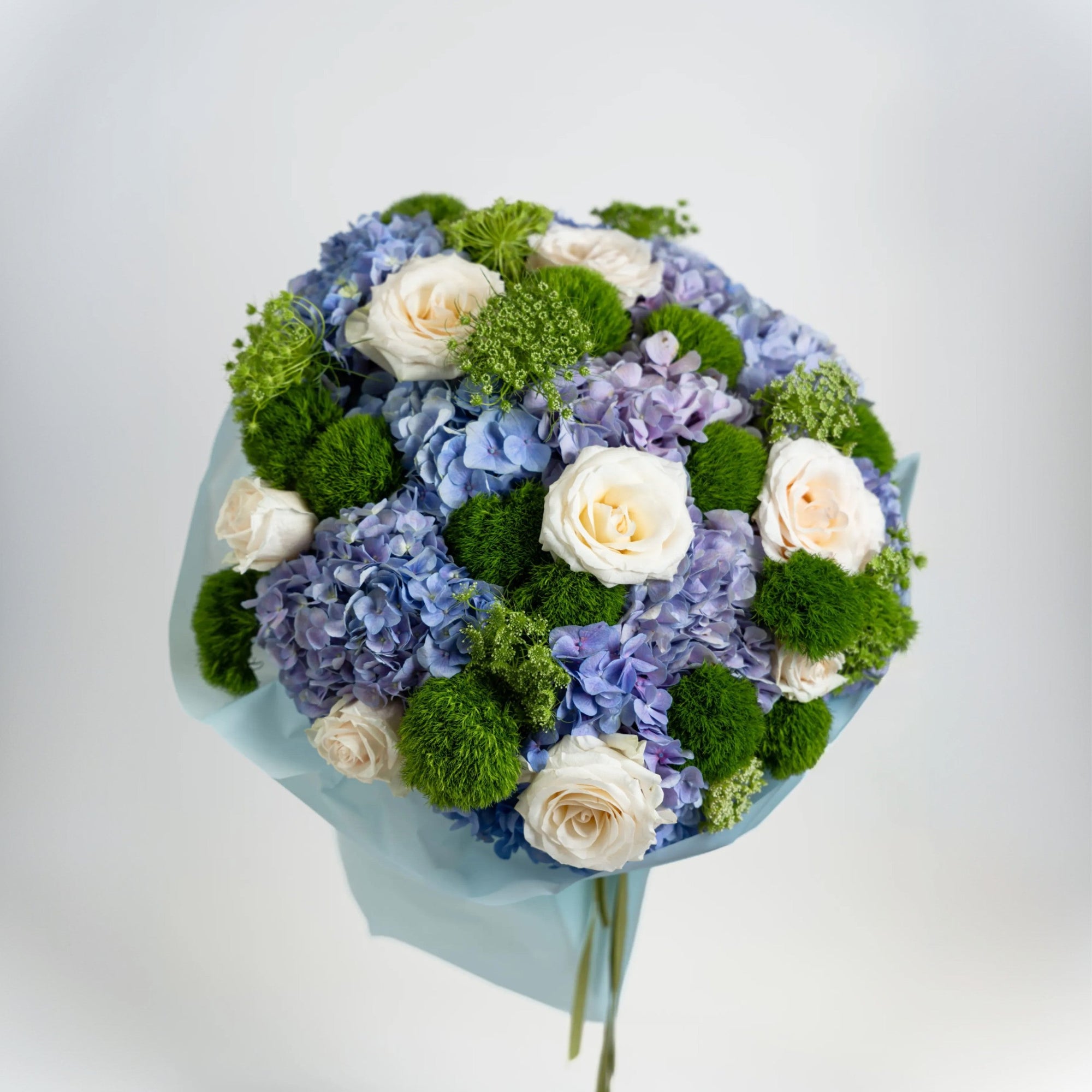 Top view of The Azure Reverie bouquet with blue hydrangeas, ivory roses and green dianthus
