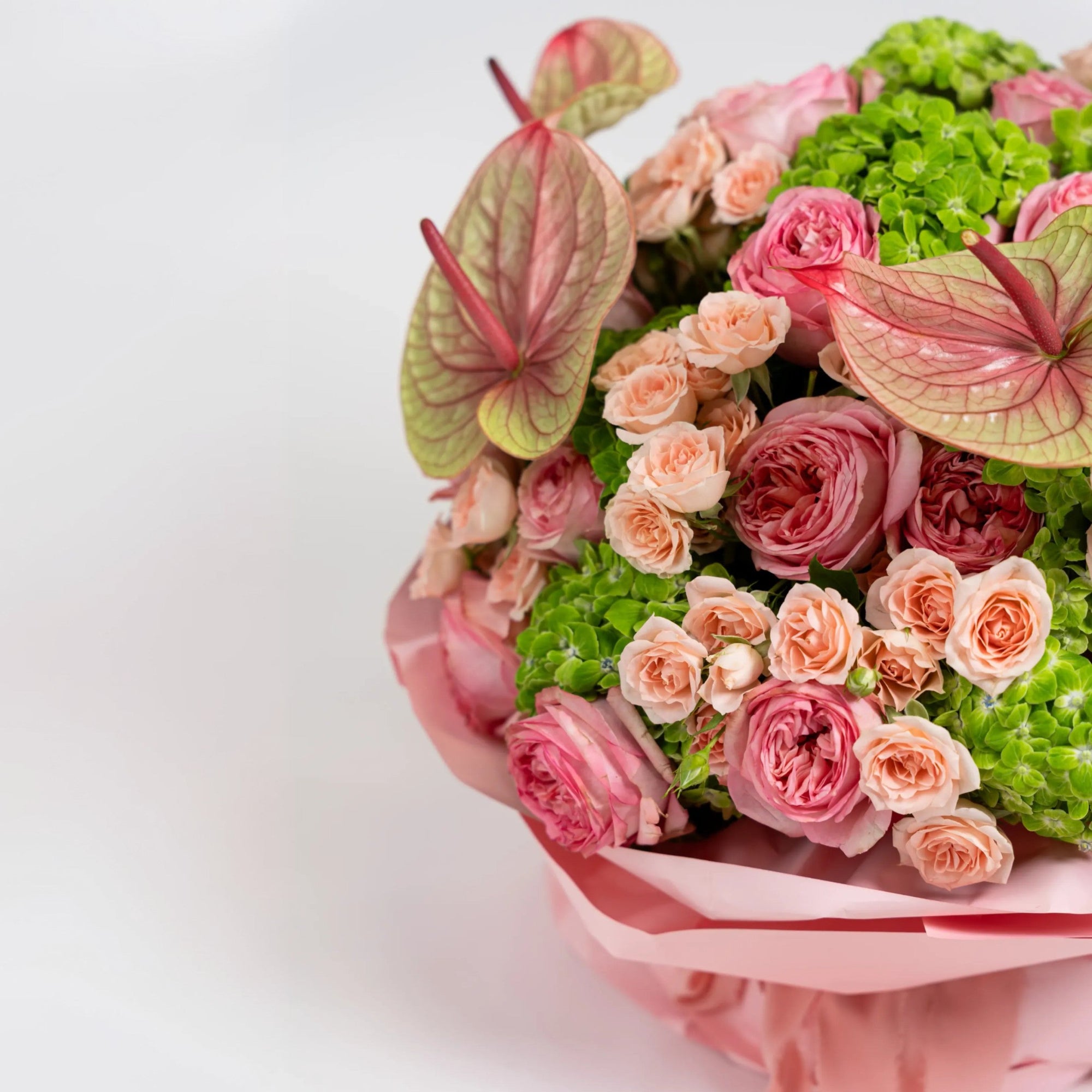 Close-up of veined pink anthuriums, garden-style roses and peach spray roses in The Eden Affair