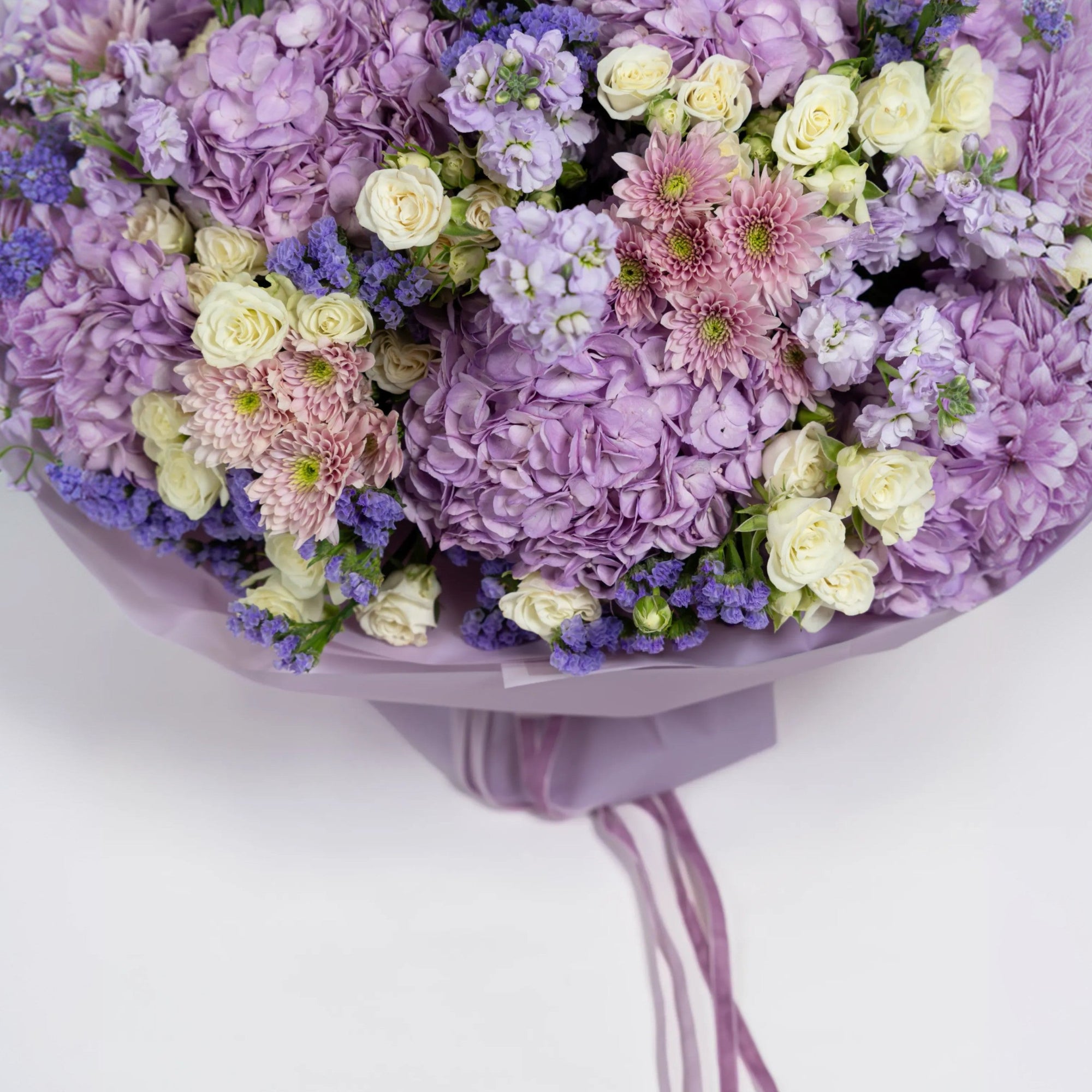 Detailed view of lilac hydrangeas, blush chrysanthemums and ivory spray roses in purple wrapping